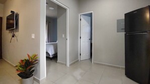 A hallway with a tiled floor, a black refrigerator, and a potted plant.