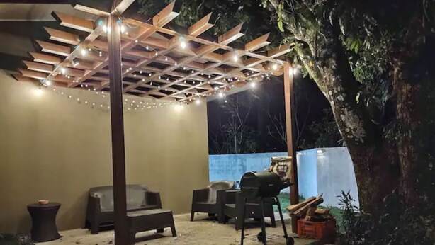 An outdoor patio area with a pergola, seating, and a barbecue grill.