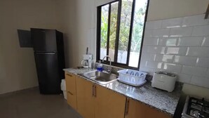 A kitchen with wooden cabinets, a stainless steel sink, a coffee maker, a toaster, and a window with a view of greenery.
