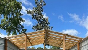 Piscina ao ar livre coberta, com deck de madeira, paredes de metal e estrutura de pérgula.