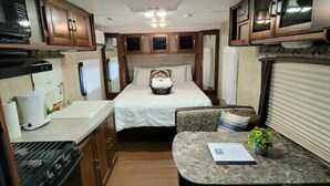 Interior compacto de uma RV com cozinha compacta, uma cama e um pequeno espaço de estar.