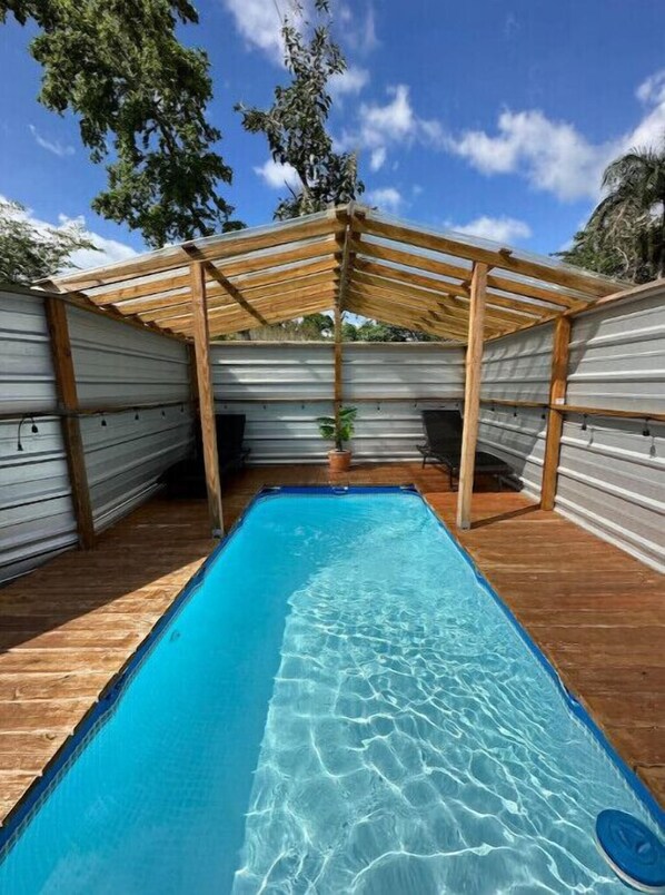 Ein rechteckiger Pool mit klarem, blauem Wasser, umgeben von Holzdeck-Terrasse und Metallwänden.