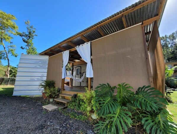 A small, single-story building with a corrugated metal roof and a covered porch. There are steps leading to the entrance, and the porch is adorned with white curtains. - El Rinconcito RV Experience 2.0! Private Pool (Rincón)