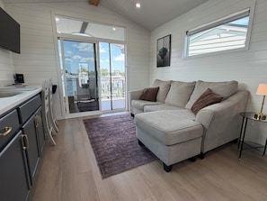 A modern living room with a grey sofa, a small side table, and a view of the outdoors through a sliding glass door.
