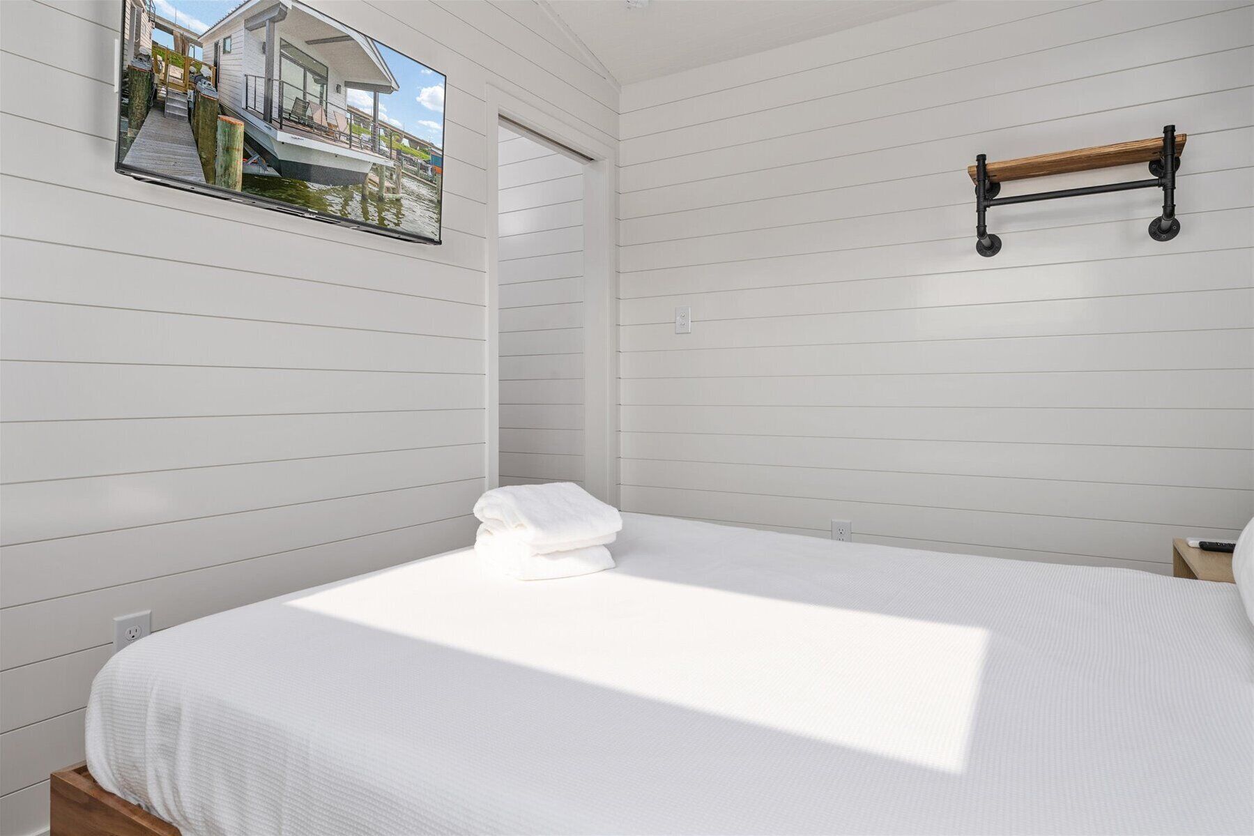 A bedroom with a bed, a wooden shelf, and a window with a view of a house and dock.
