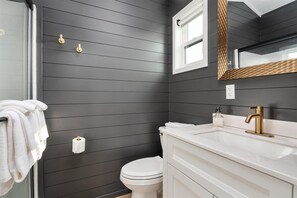 A bathroom with dark wood paneling, a white toilet, a white sink with gold fixtures, and a mirror with a woven frame.