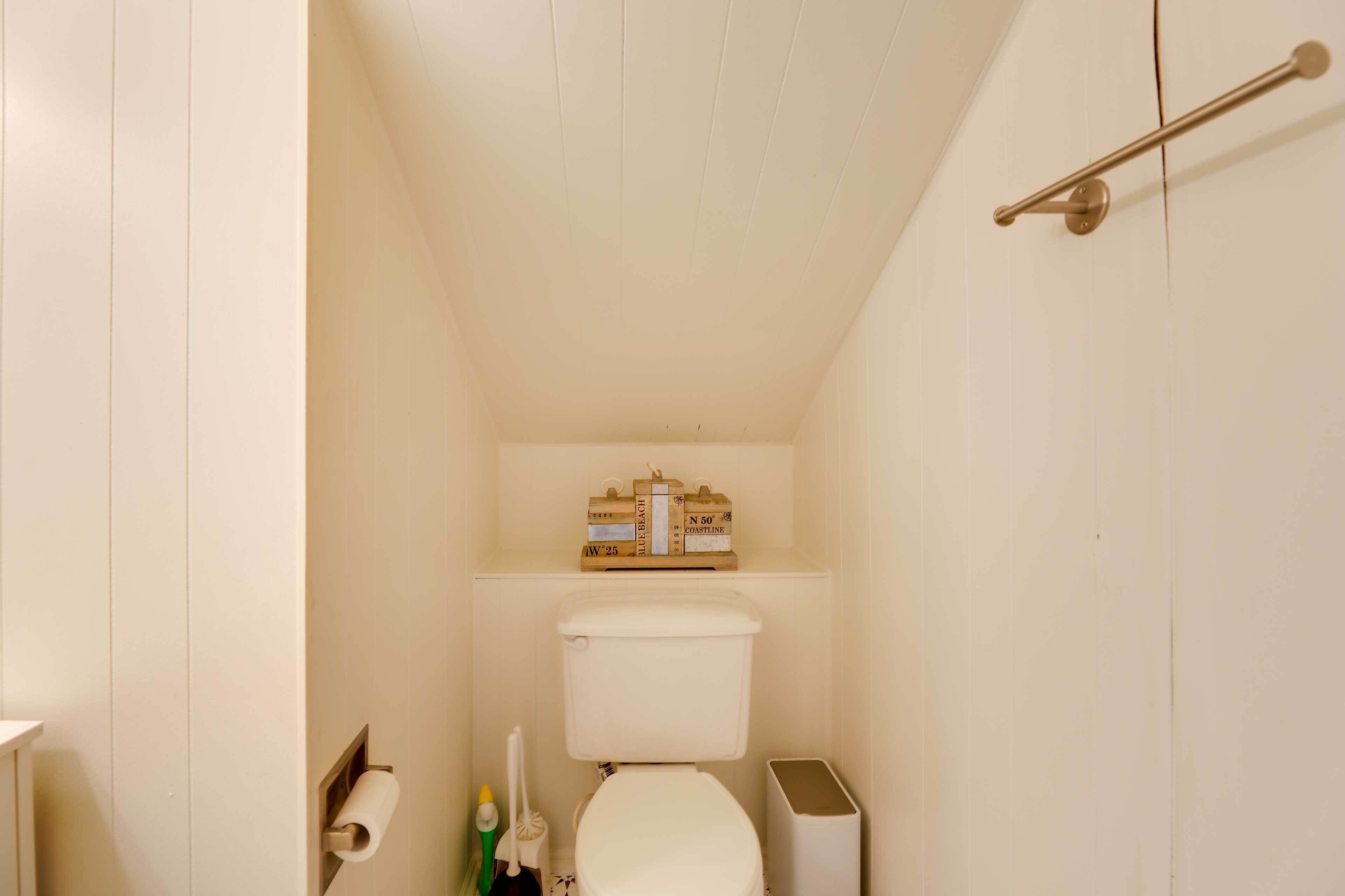 A small, white bathroom with a toilet, a shelf above the toilet holding boxes, a toilet paper holder, and a hand dryer.