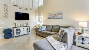 A living room with a grey sofa, a TV mounted on the wall, and a painting above the sofa. - Walk to Beach! PCB Resort Condo w/ Pool Access (Panama City Beach)