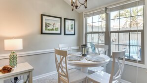 A dining area with a round table, white chairs, a lamp, and two framed pictures on the wall. - Walk to Beach! PCB Resort Condo w/ Pool Access (Panama City Beach)