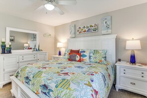 Ein Schlafzimmer mit Bett, Nachttischen, Kommode, Deckenventilator und Wandbildern.