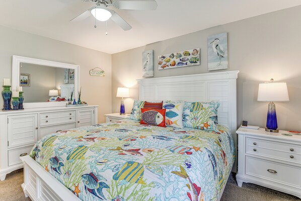 A bedroom with a bed, nightstands, a dresser, a ceiling fan, and wall art. - Walk to Beach! PCB Resort Condo w/ Pool Access (Panama City Beach)