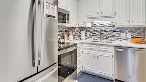 A modern kitchen with white cabinets, stainless steel appliances, a tiled backsplash, and a blue rug. - Walk to Beach! PCB Resort Condo w/ Pool Access (Panama City Beach)
