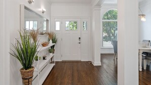 Un couloir avec une porte blanche, un plancher en bois et une plante sur le côté gauche.