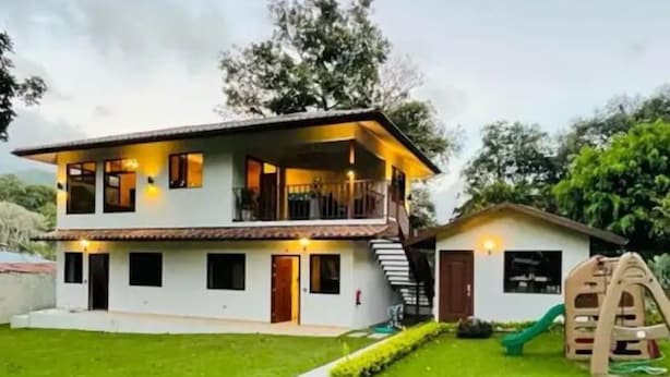 A two-story house with a balcony, a small play area with a slide, and a well-maintained lawn.