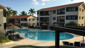A pool area with lounge chairs and umbrellas, surrounded by multi-story buildings with balconies. - THE ROYAL SUITES - WALKING DISTANCE TO 8 BEACHES - ALL INCLUSIVE (Cofresi)