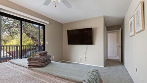 A bedroom with a large bed, a flat-screen TV mounted on the wall, and a balcony with a view of trees and a car. - ✨ 3-King Beds / HotTub / EV Charger / Mountain View / Walk to River & Dining (Three Rivers)