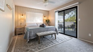 A bedroom with a bed, bedside table, bench, and a view of the outdoors through a sliding glass door. - ✨ 3-King Beds / HotTub / EV Charger / Mountain View / Walk to River & Dining (Three Rivers)