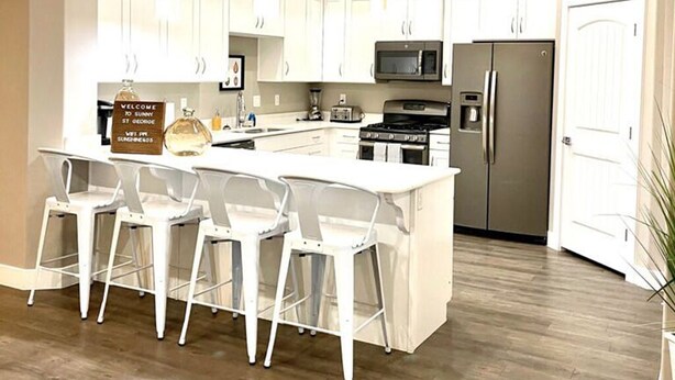 A modern kitchen with white cabinetry, a central island with bar stools, stainless steel appliances, and a ceiling fan.