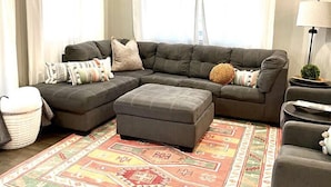 A modern living room with a sectional sofa, ottoman, and a patterned rug.
