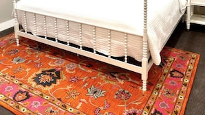 A four-poster bed with a white frame, a colorful rug, and a ceiling fan.