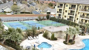 A resort with multiple swimming pools, a tennis court, and a view of mountains in the background.