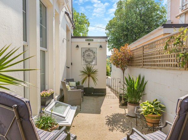 A sunlit patio with outdoor seating, a potted plant, and a framed sign on the wall. - The Hideaway at The Morley (Torquay)