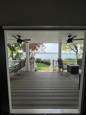 Une terrasse couverte avec vue sur un lac, comprenant un espace salon extérieur et un ventilateur de plafond.