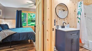 Una habitación de madera con una cama, un baño con lavamanos y una ventana con cortinas.