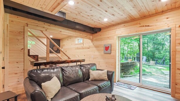 Interior acogedor de una cabaña con un sofá de cuero, una mesa de comedor y un amplio ventanal con vistas al exterior.