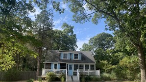 A two-story house with a front porch, surrounded by trees and a fenced yard. - Catherine’s Place (Southampton)