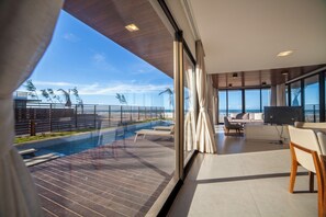 A modern living room with a large window overlooking a pool and ocean view. - ILLA BLUE VILLAGE (Trairi)