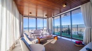 A spacious living room with a large window overlooking the beach, a wooden ceiling, and a modern sofa set. - ILLA BLUE VILLAGE (Trairi)