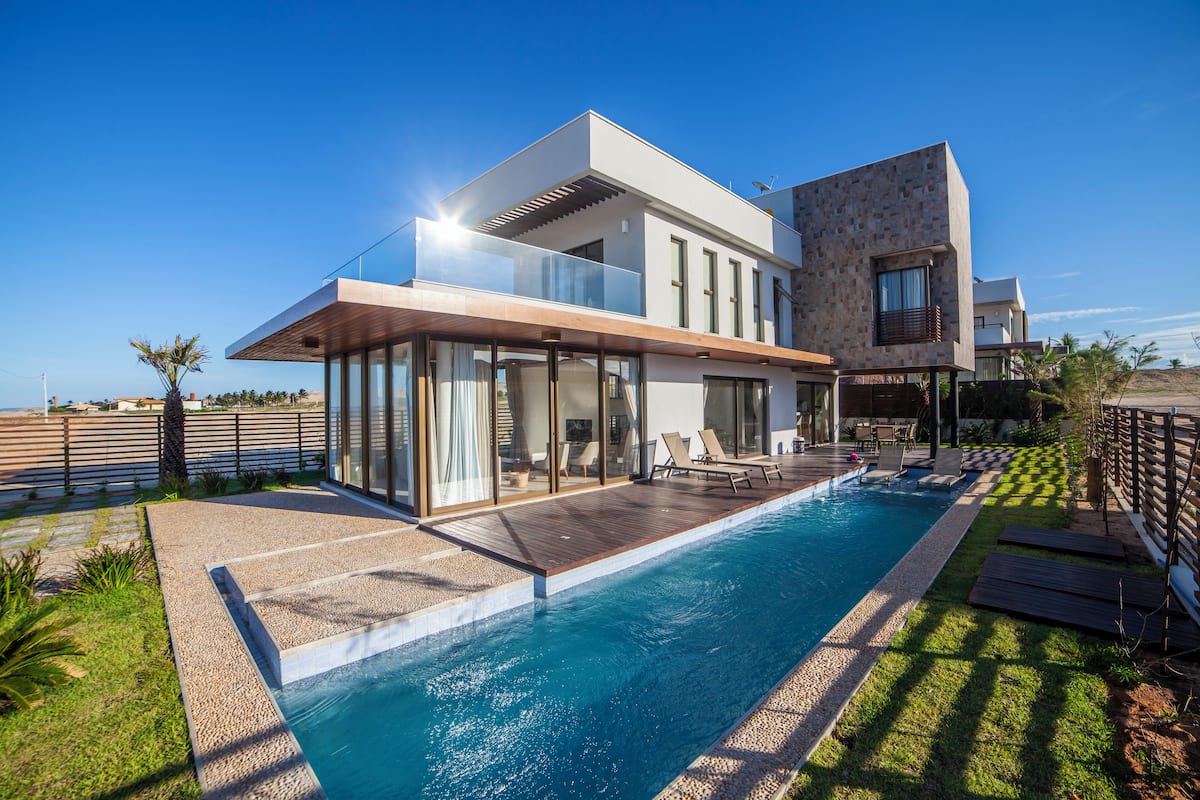 A modern two-story house with a swimming pool, large glass windows, and a wooden deck.