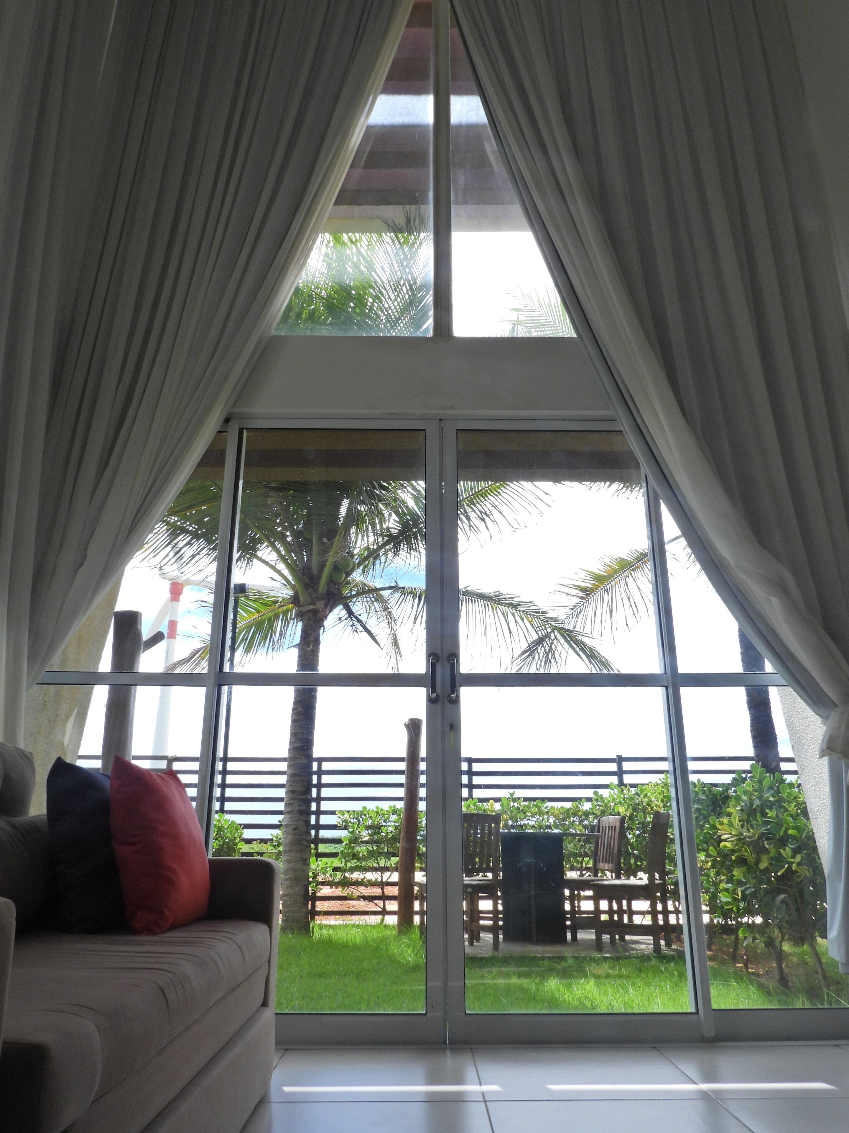 A room with a large sliding glass door leading to a balcony with a view of palm trees and a fence.