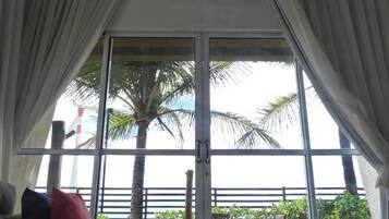 A room with a large sliding glass door leading to a balcony with a view of palm trees and a fence.