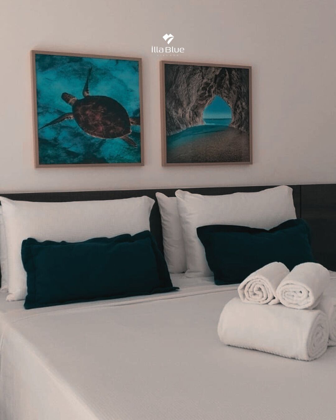 Une chambre d’hôtel avec un lit, deux oreillers, deux œuvres d’art encadrées et des serviettes roulées.