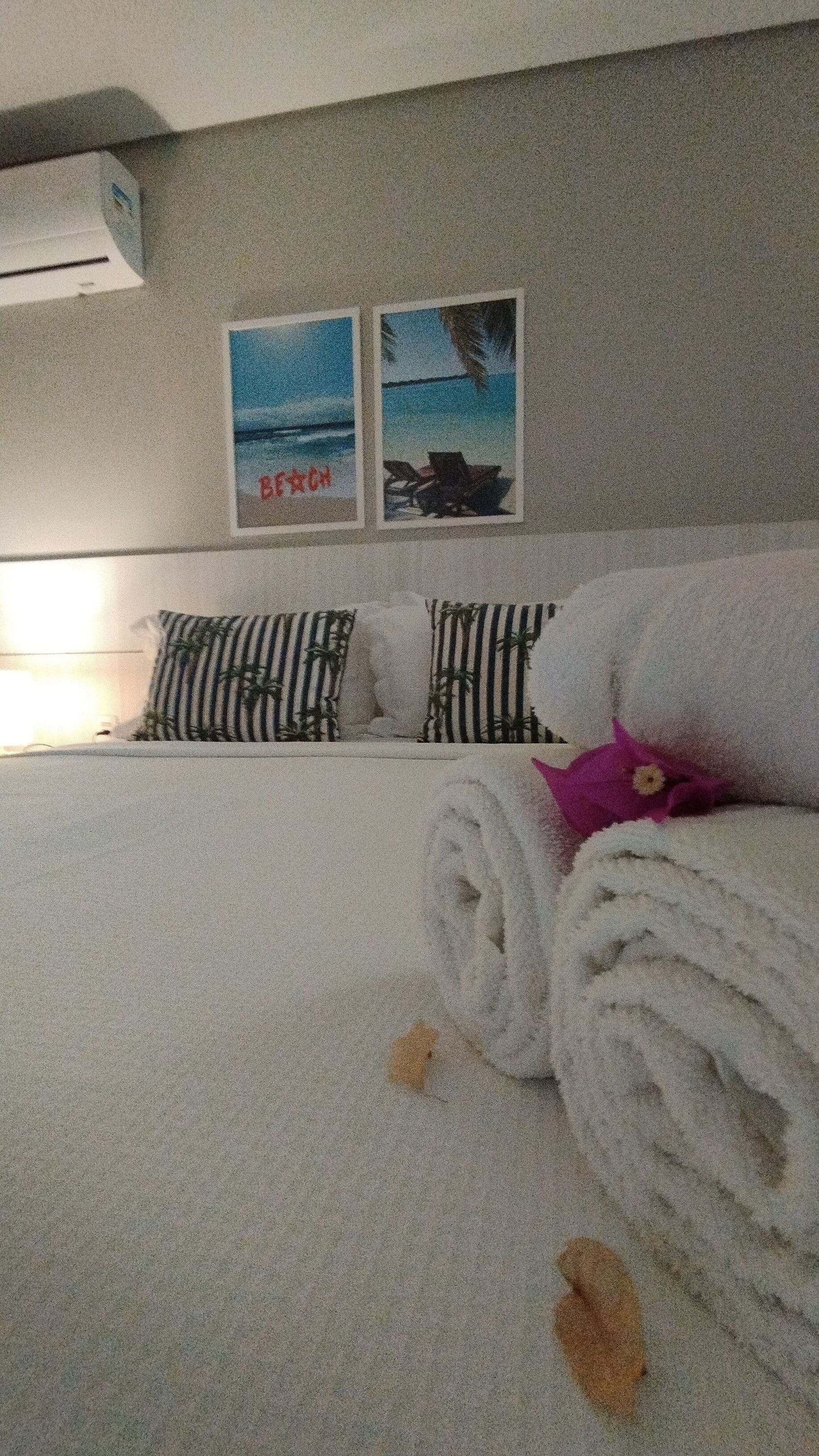 A hotel room with a bed, pillows, and two wall art pieces depicting beach scenes.