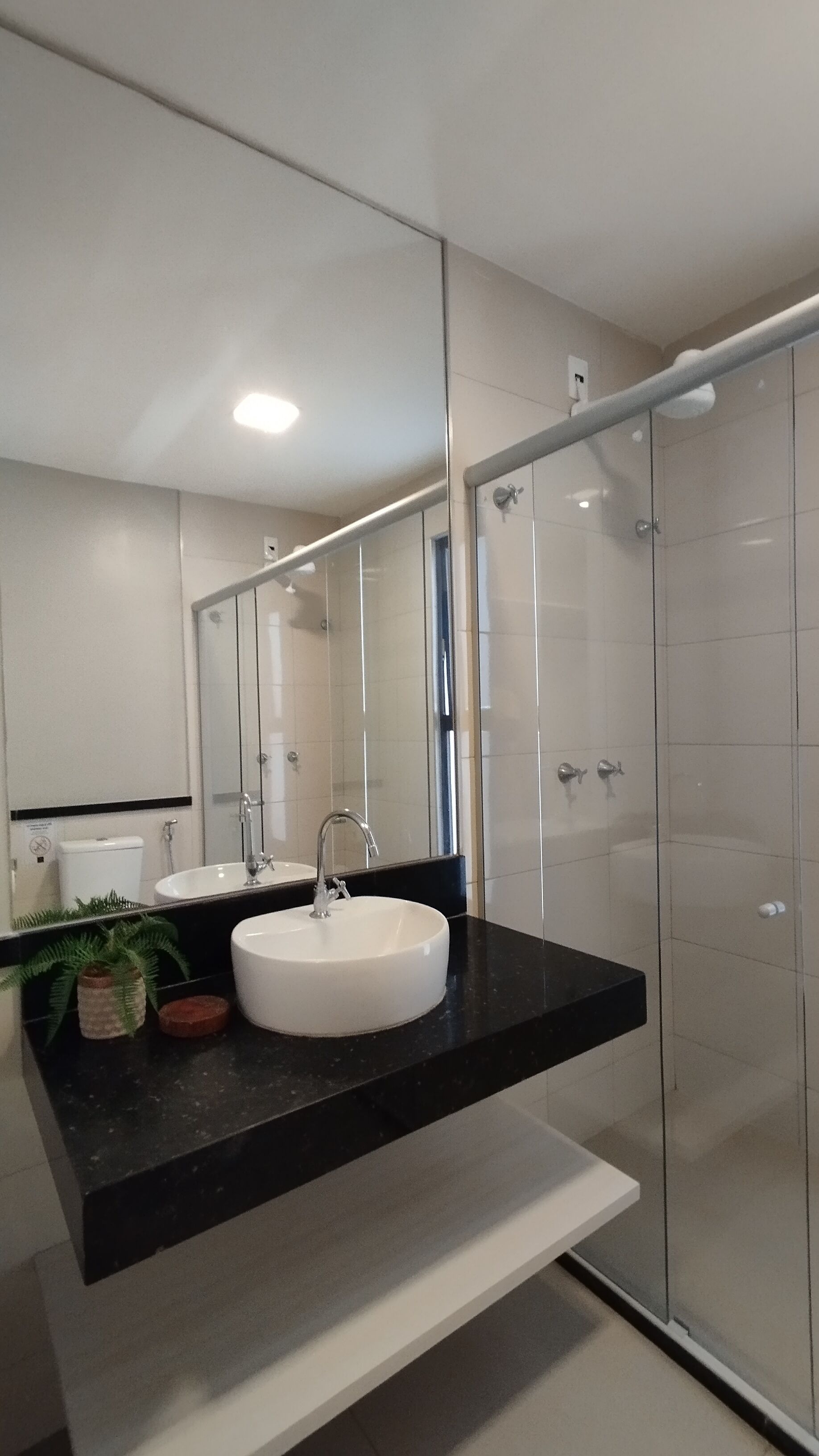 A modern bathroom with a white sink, black countertop, and a glass shower enclosure.