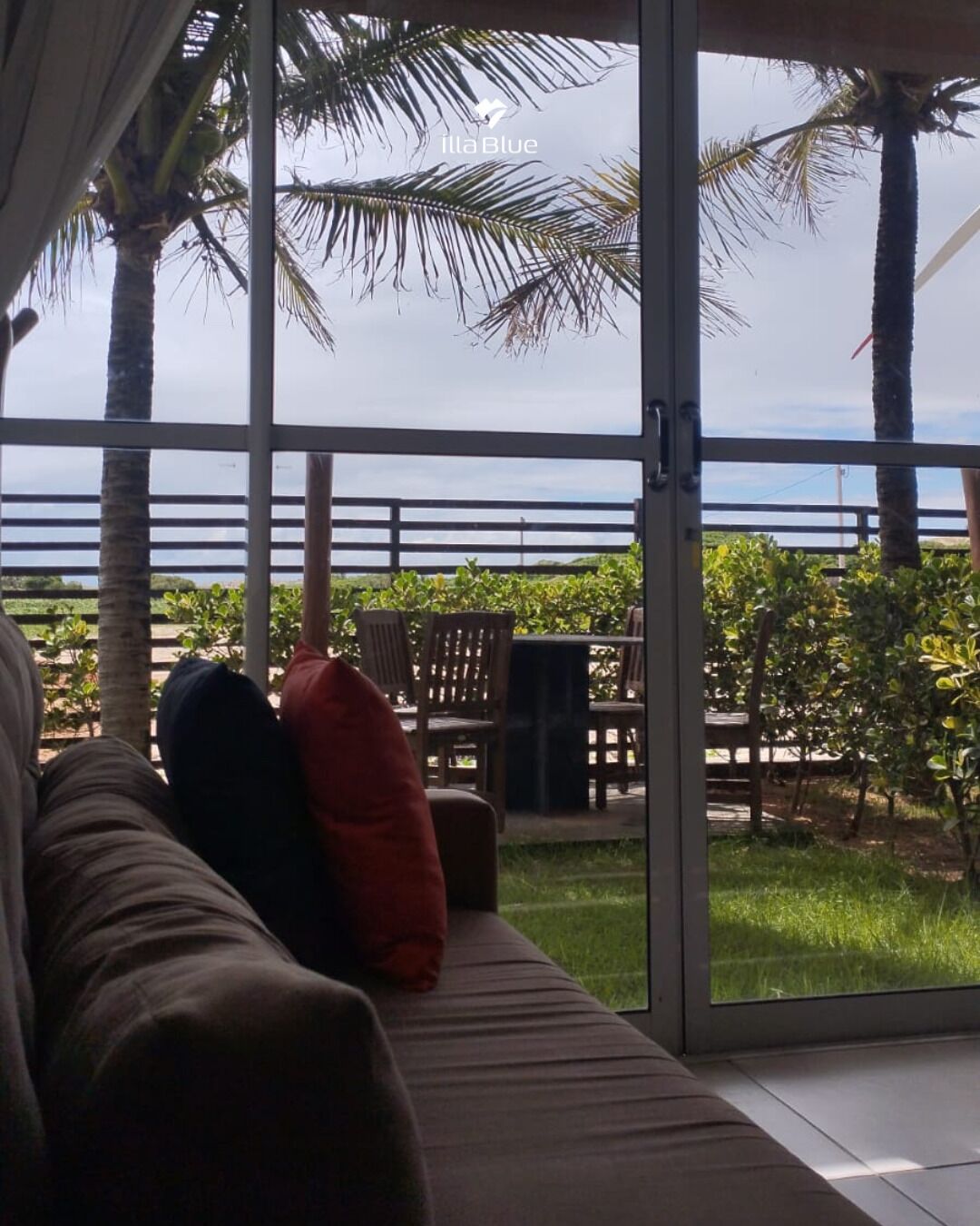 A room with a glass door leading to a balcony with outdoor furniture and palm trees.