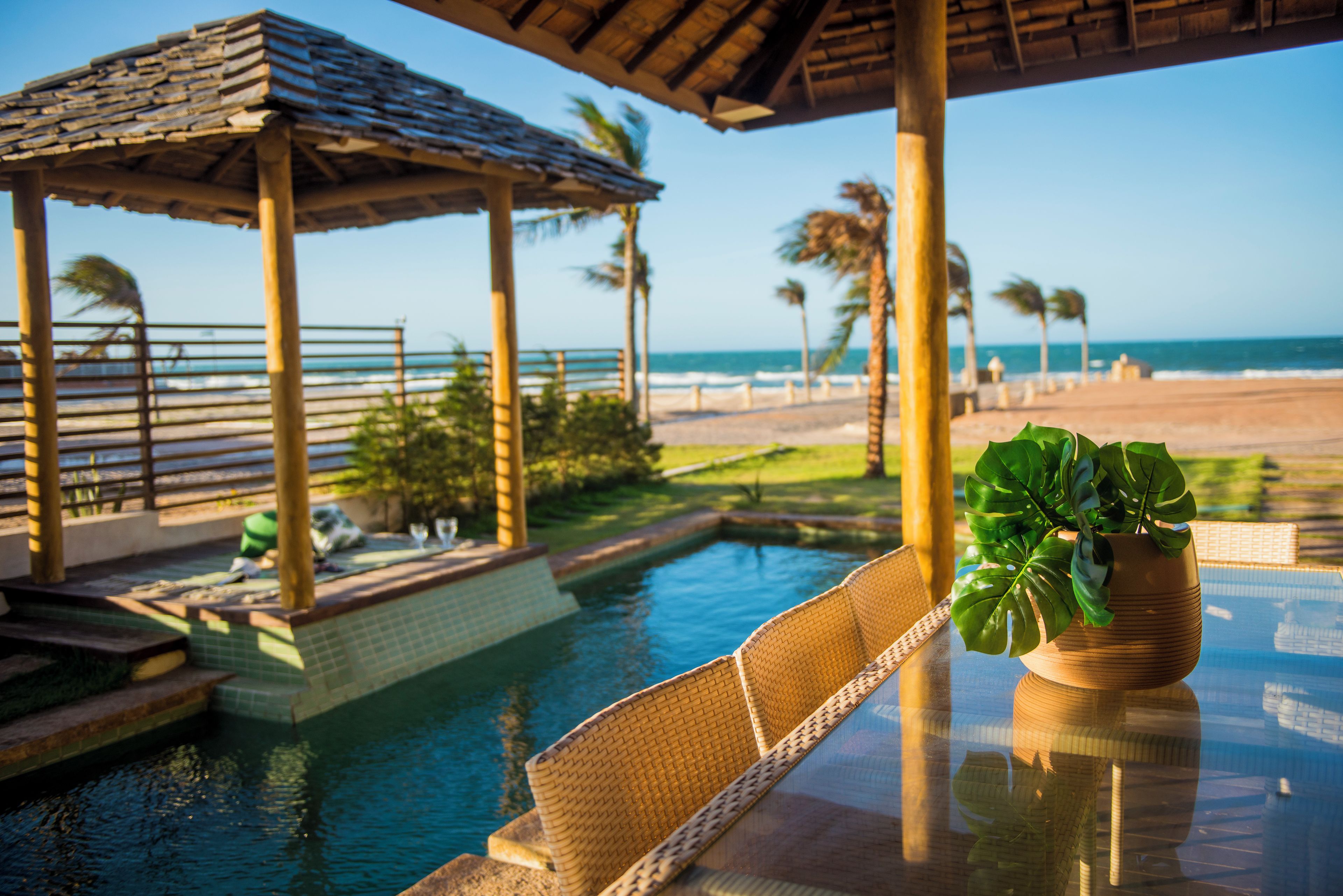 A pool area with a lounge chair, a potted plant, and a view of the beach and ocean.