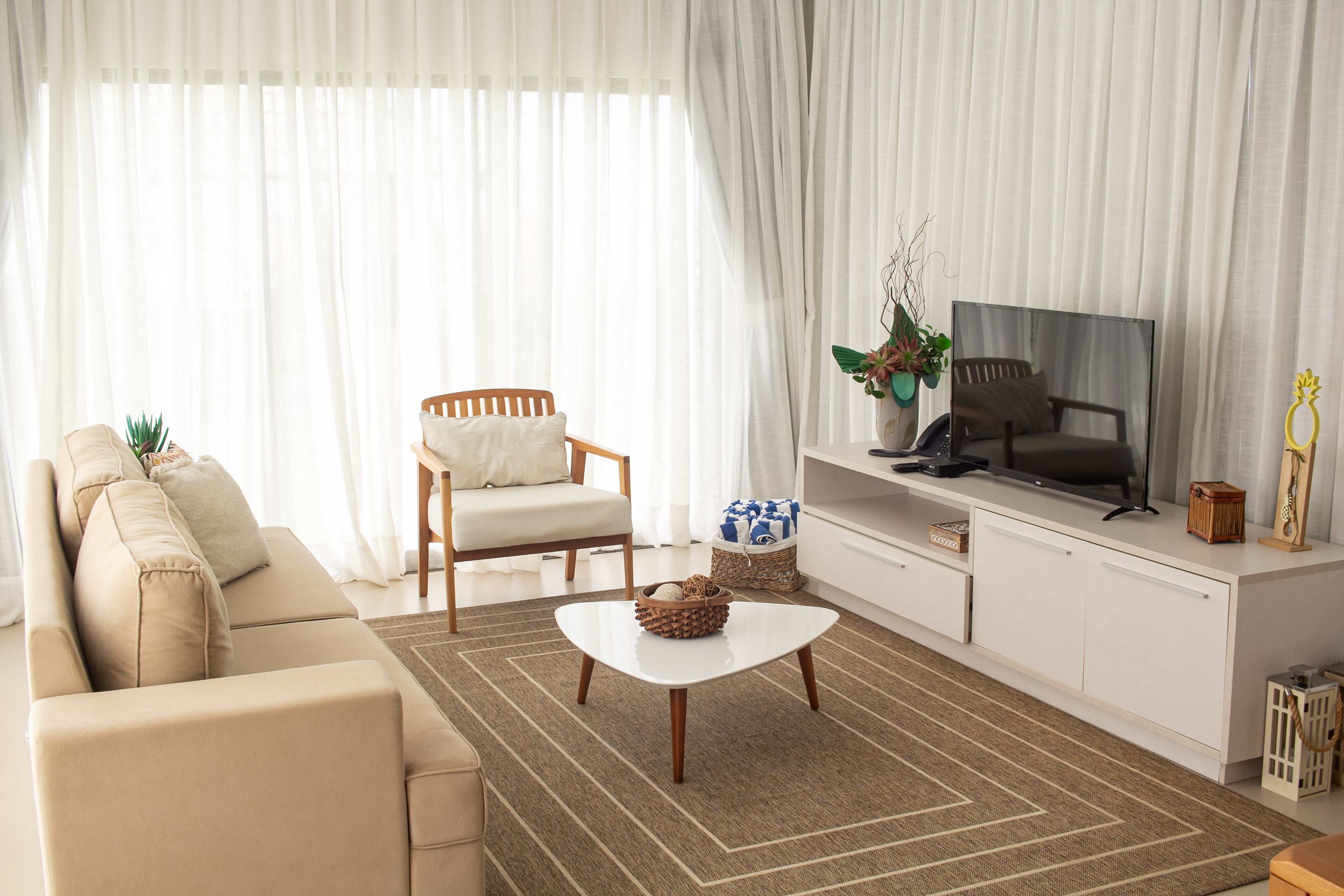Una sala de estar con sofá, sillón, mesa de centro, televisor y cortinas.