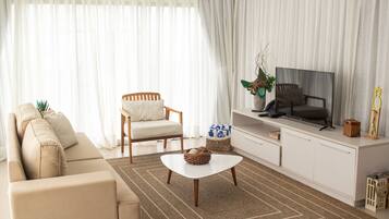 Una sala de estar con sofá, sillón, mesa de centro, televisor y cortinas.
