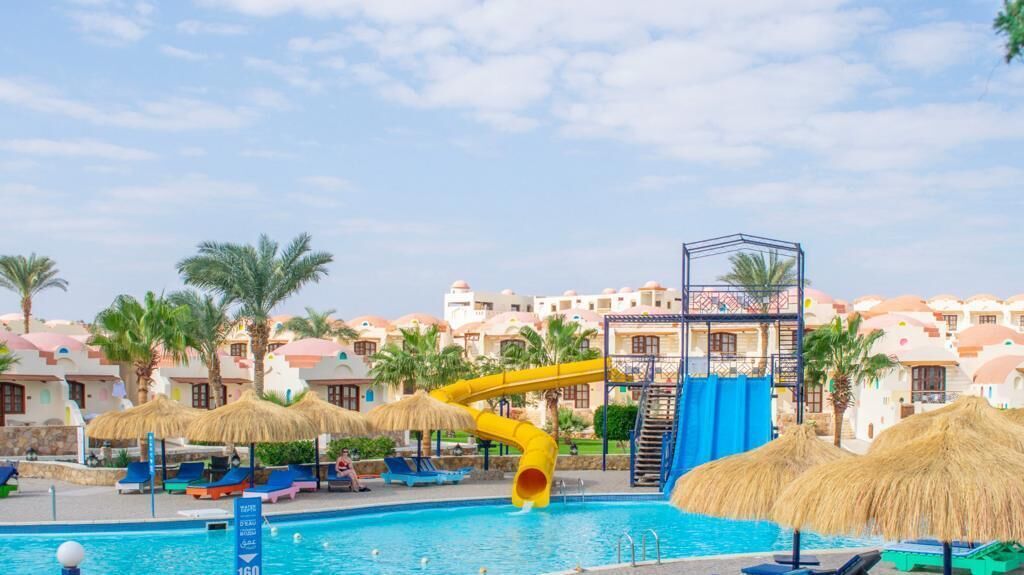 A swimming pool with a yellow water slide, lounge chairs, and thatched umbrellas.