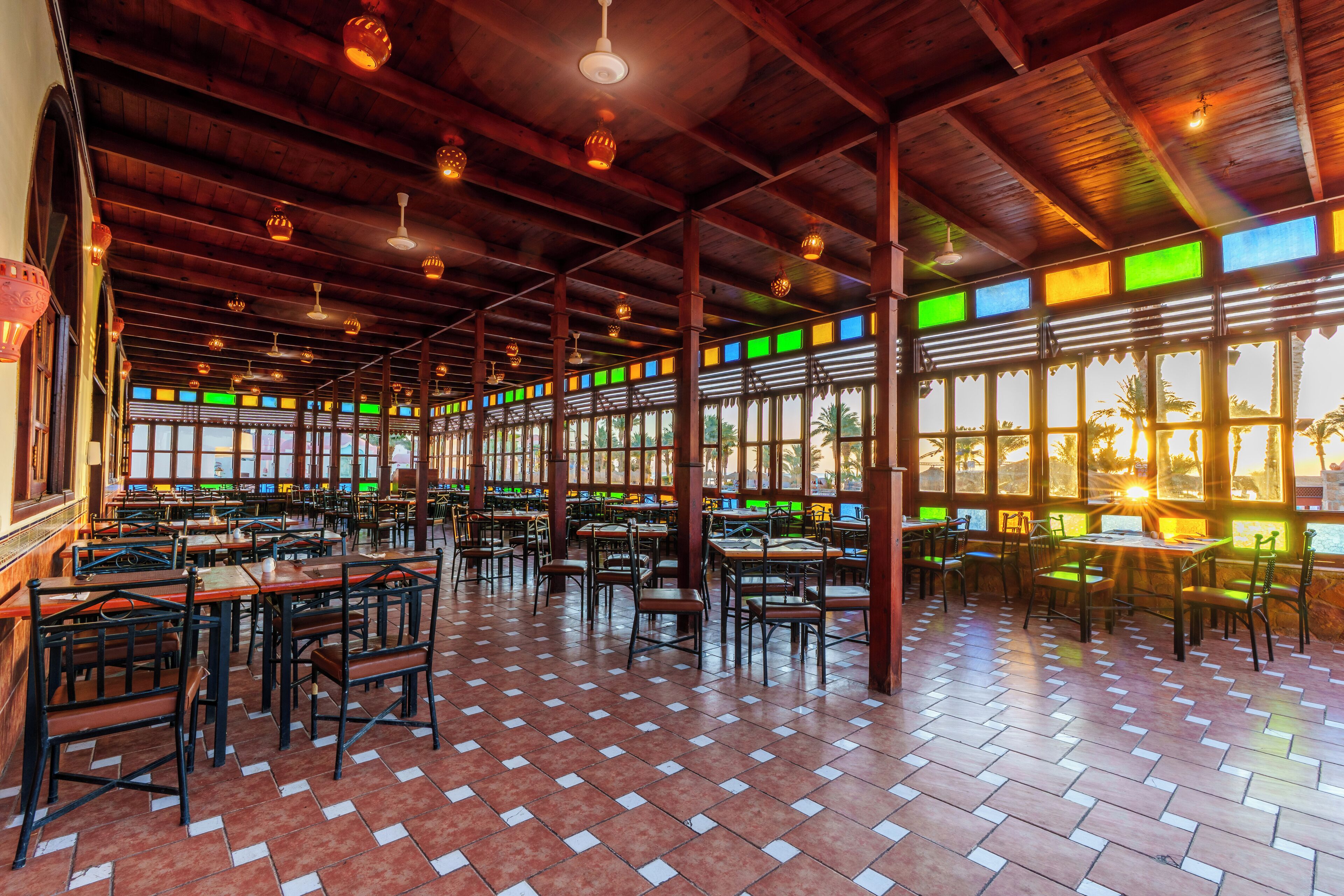 A spacious indoor dining area with wooden beams and tiled flooring, featuring multiple tables and chairs.