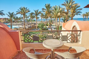 Ein Balkon mit Korbmöbeln mit Blick auf einen Poolbereich, Palmen und Meer.