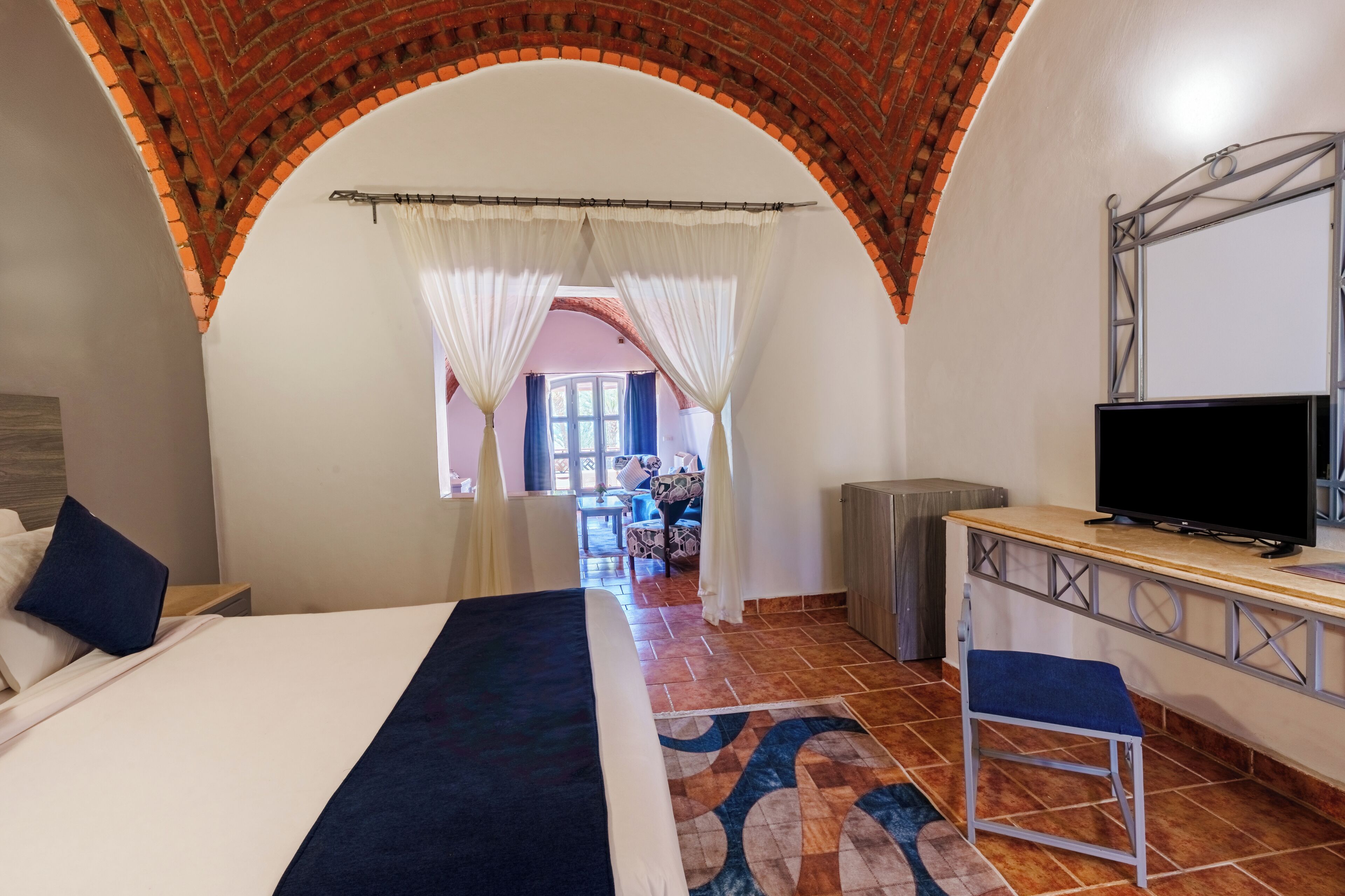 A hotel room with a bed, a TV, a desk, and an arched brick ceiling.