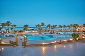Ein Poolbereich eines Resorts mit mehreren Schwimmbecken, Palmen und Liegestühlen.