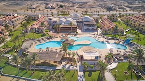 Eine Luftaufnahme eines Resorts mit mehreren Schwimmbecken, Palmen und einer Wüstenlandschaft im Hintergrund.