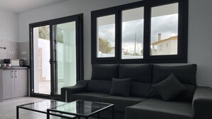 Una sala de estar moderna con un sofá gris oscuro, una mesa de centro de vidrio y una cocina con microondas y armarios.
