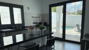 Una cocina moderna con una isla central, taburetes de bar y vista a una piscina.